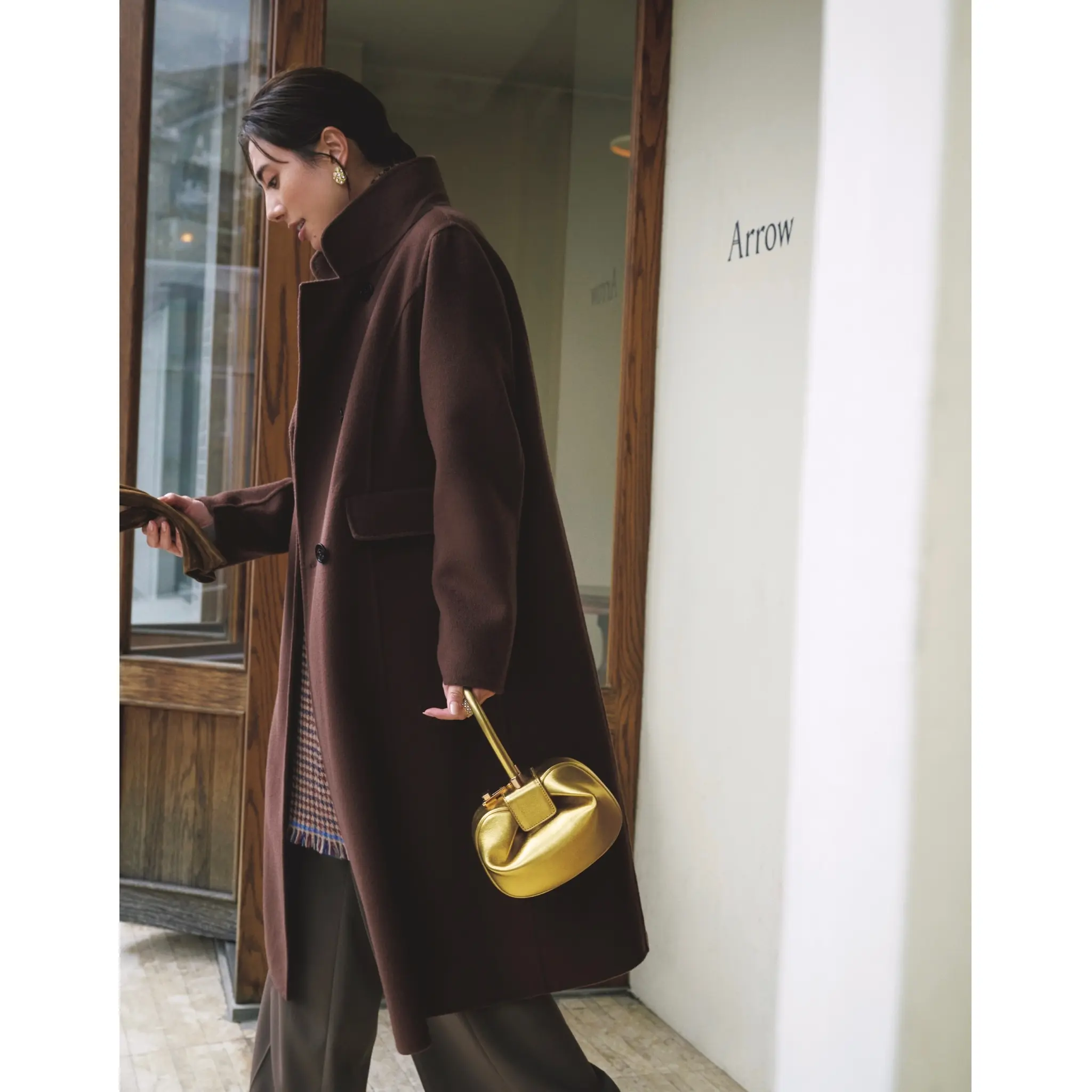 ブラウンのチェスターコートにブラウンパンツを合わせ、ゴールドのミニバッグを持ったコーディネート　モデル・土屋巴瑞季