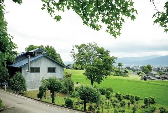 三角屋根の水色の一軒家が鈴木さんが暮らし、ガラス制作を行うスタジオ。南側には芝生の庭が設けられ、その向こうには散居村の風景が広がる。