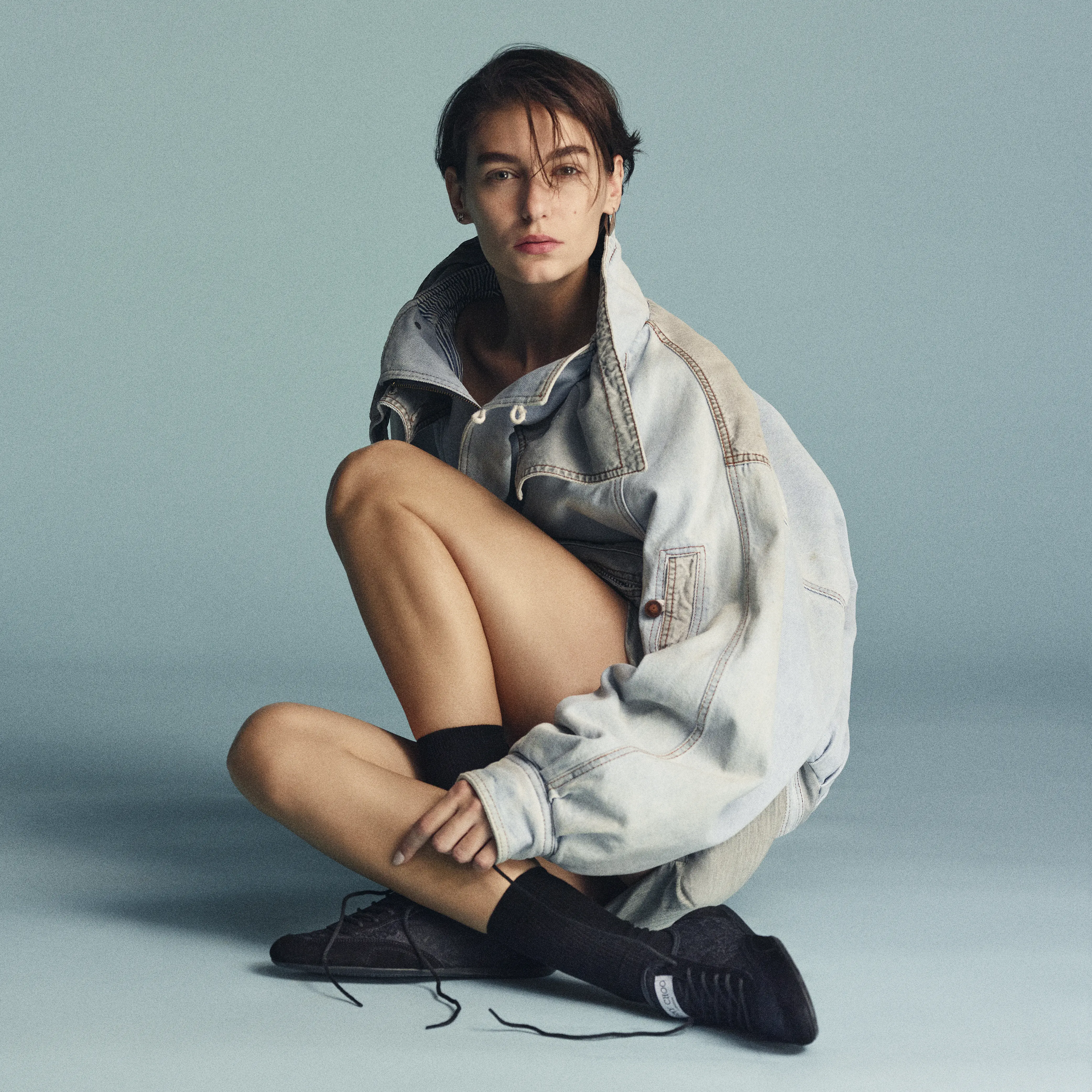 黒レーススニーカー ジミー チュウ「SUNNY」を履いた女性モデルの写真。モデルはライトブルーのデニムジャケットとグレーミニスカートを合わせたコーディネート