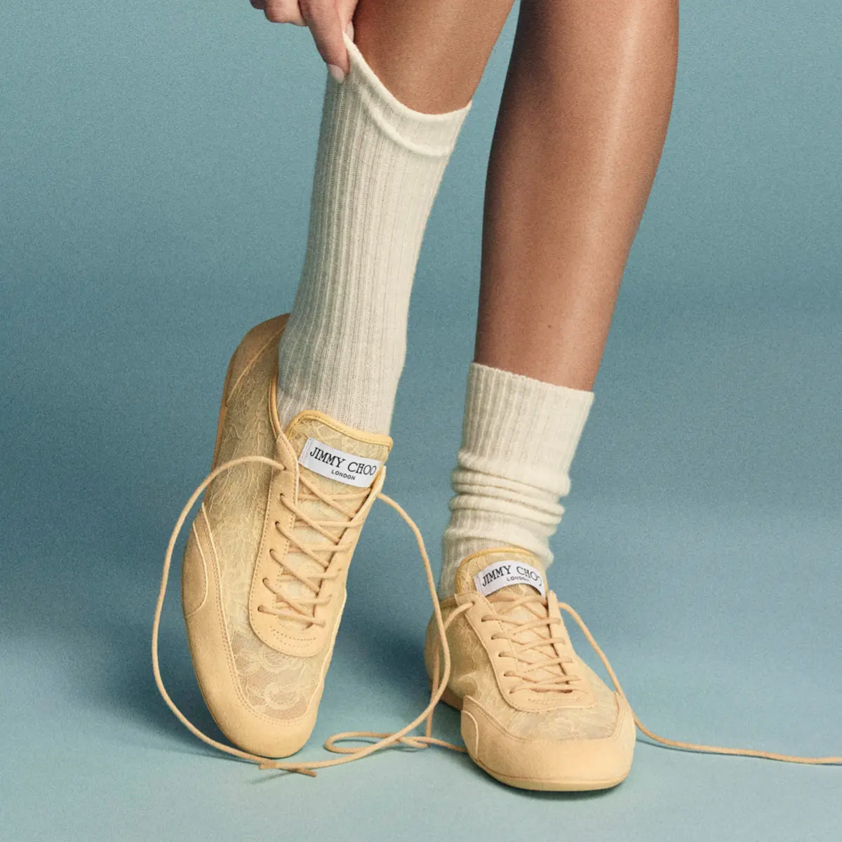 ベージュレーススニーカー ジミー チュウ「SUNNY」を履いた女性モデルの足元の写真。スニーカーには白ソックスを合わせている。