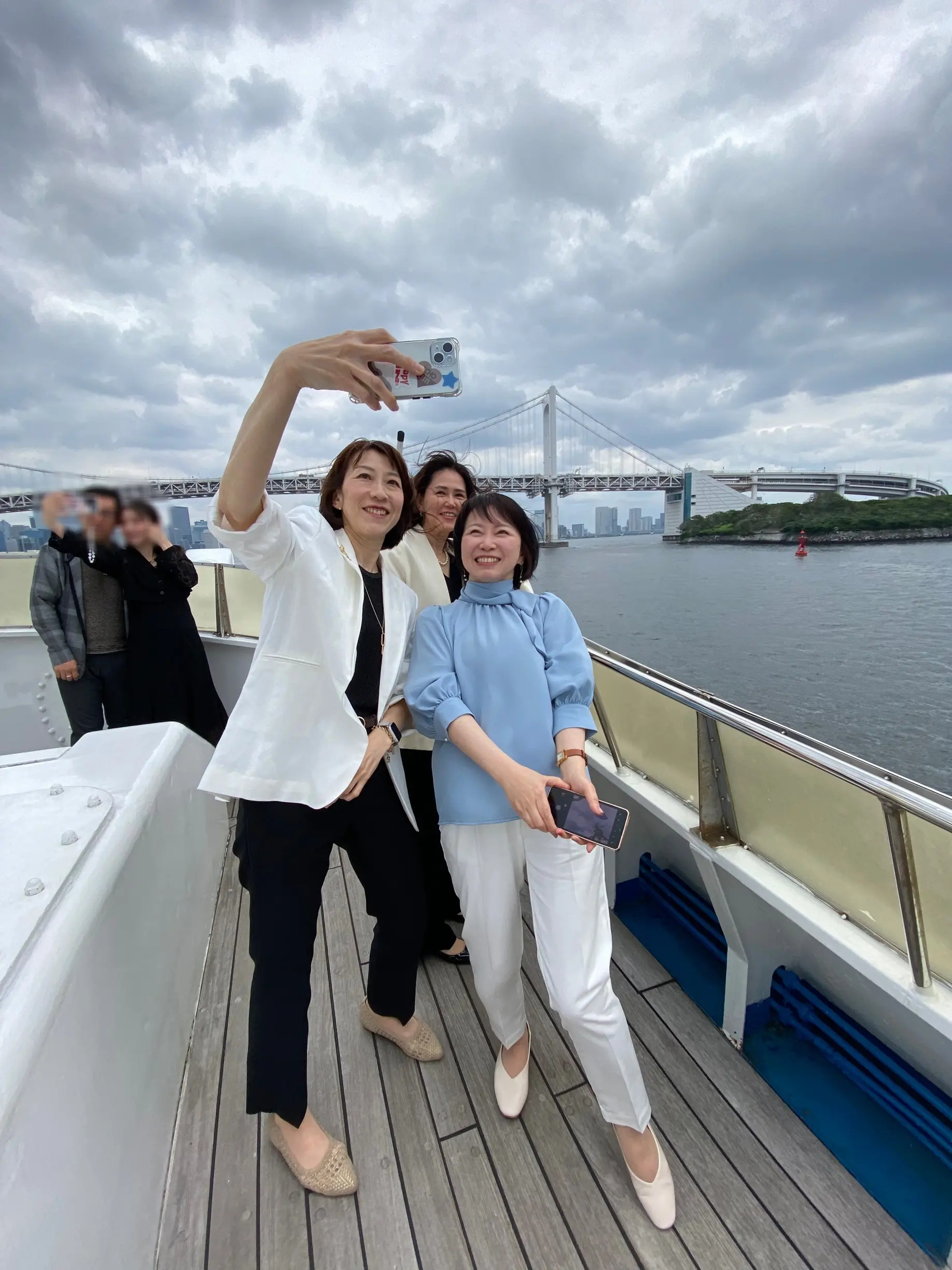 海と橋を背景に、自然な笑顔で写真を撮り合うJマダムたち