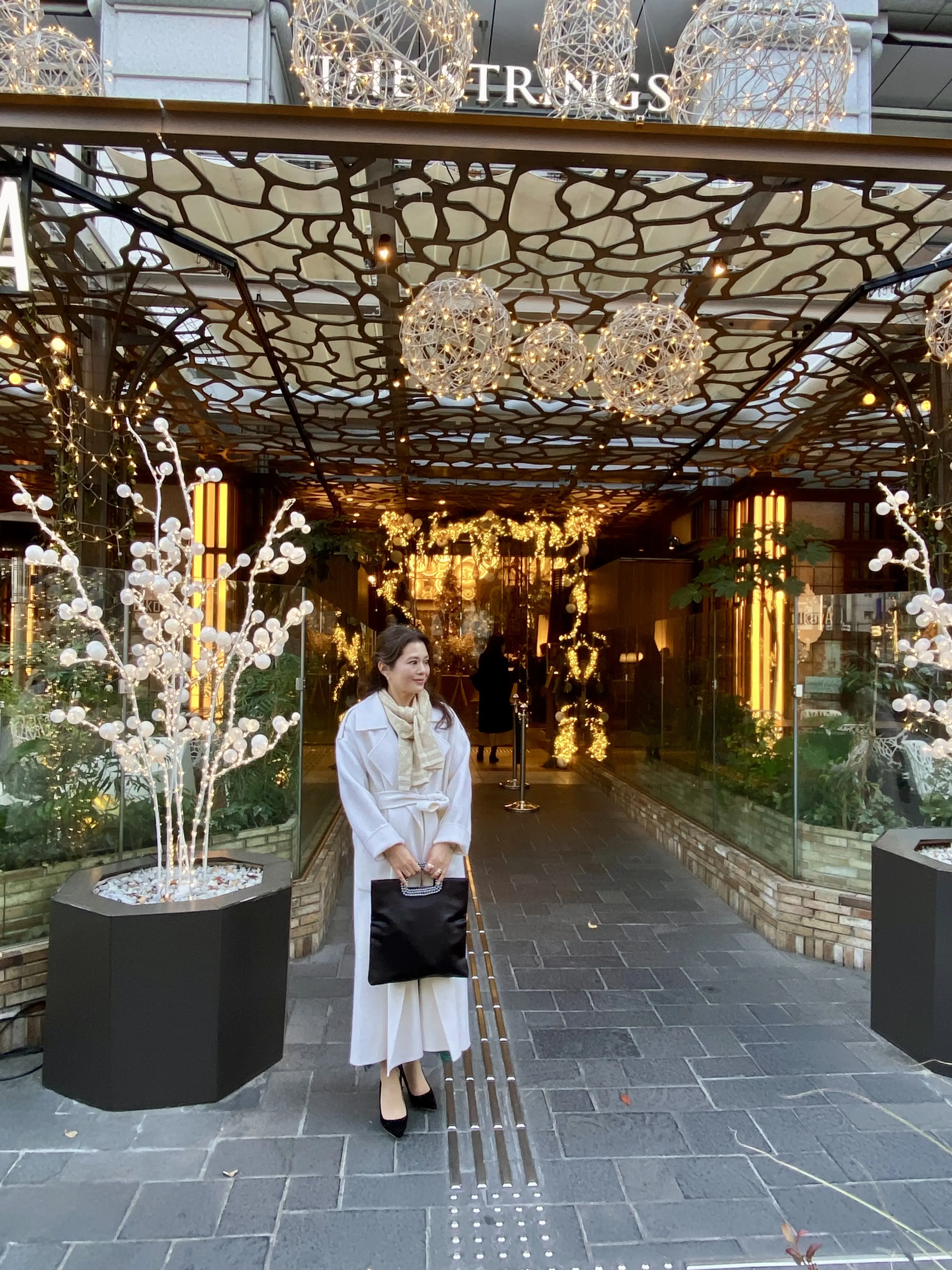 2025年ソワレ・ドゥ・エクラ、ザストリングス表参道前で撮影。イルミネーションに包まれた白コートコーデの筆者