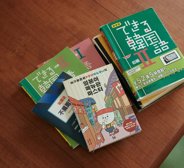 メインで使っているのは『できる韓国語』シリーズ(アスク出版)。現在は「初級Ⅱ」を学んでいる。イラストが表紙の本は、韓国語の先生に初めて会ったときにもらった『マグロせんせいの日本語メニューマスター』。