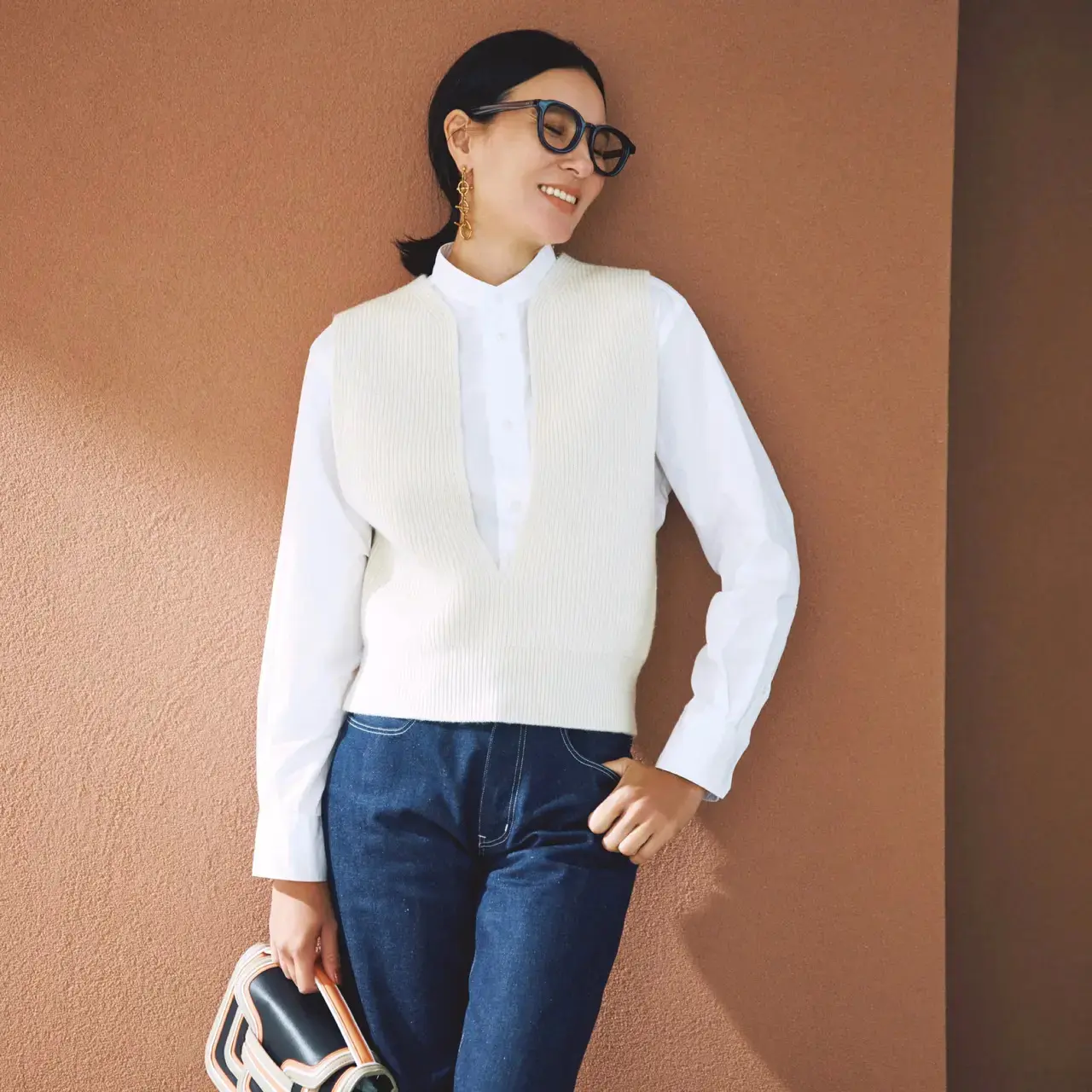 胸元の深いスリットデザインがニットベスト×シャツの装いにスタイリッシュな印象を授ける。