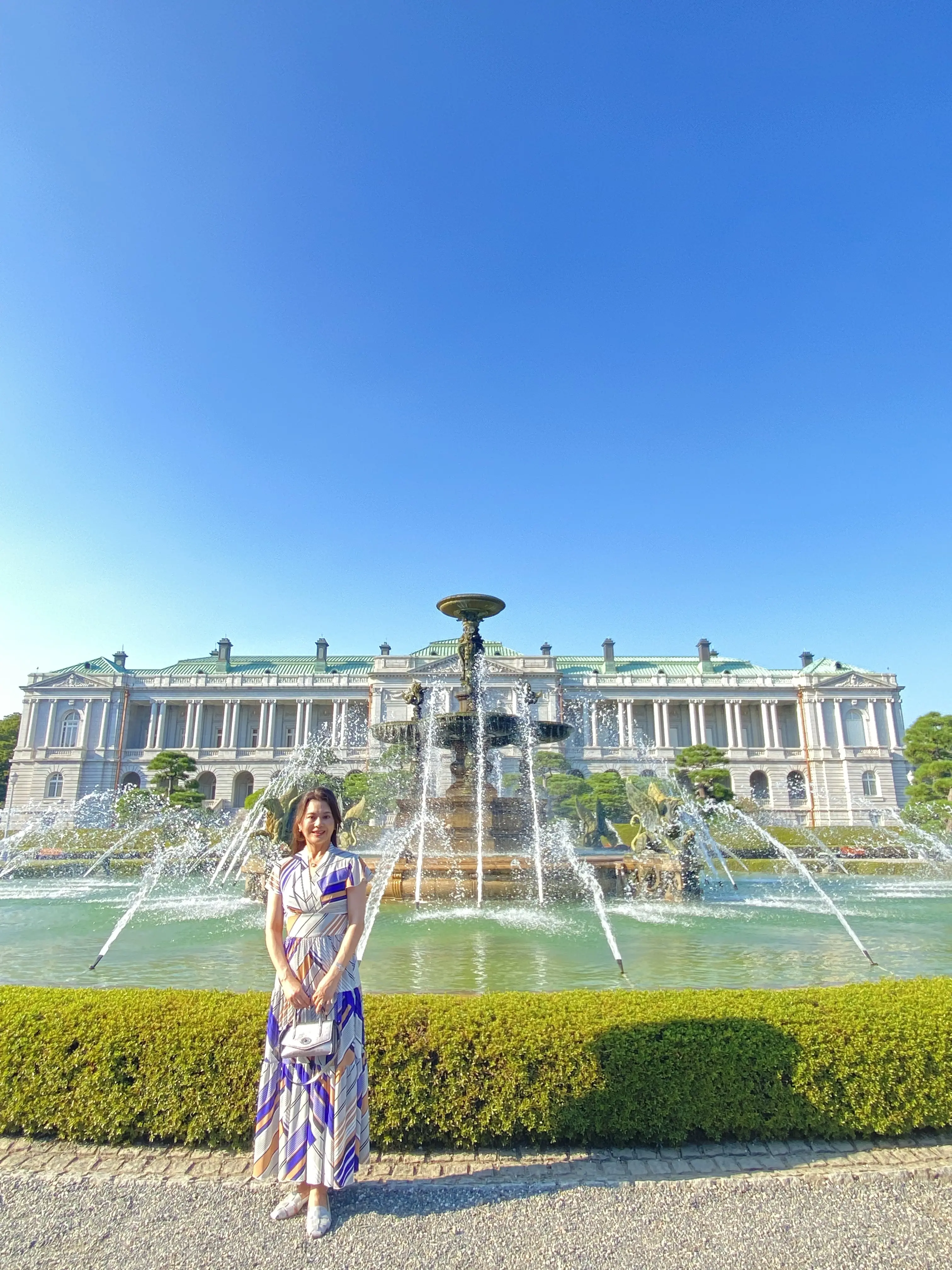 迎賓館の噴水前でポーズをとる女性。ワンピースと背景の建物が美しくマッチしている。