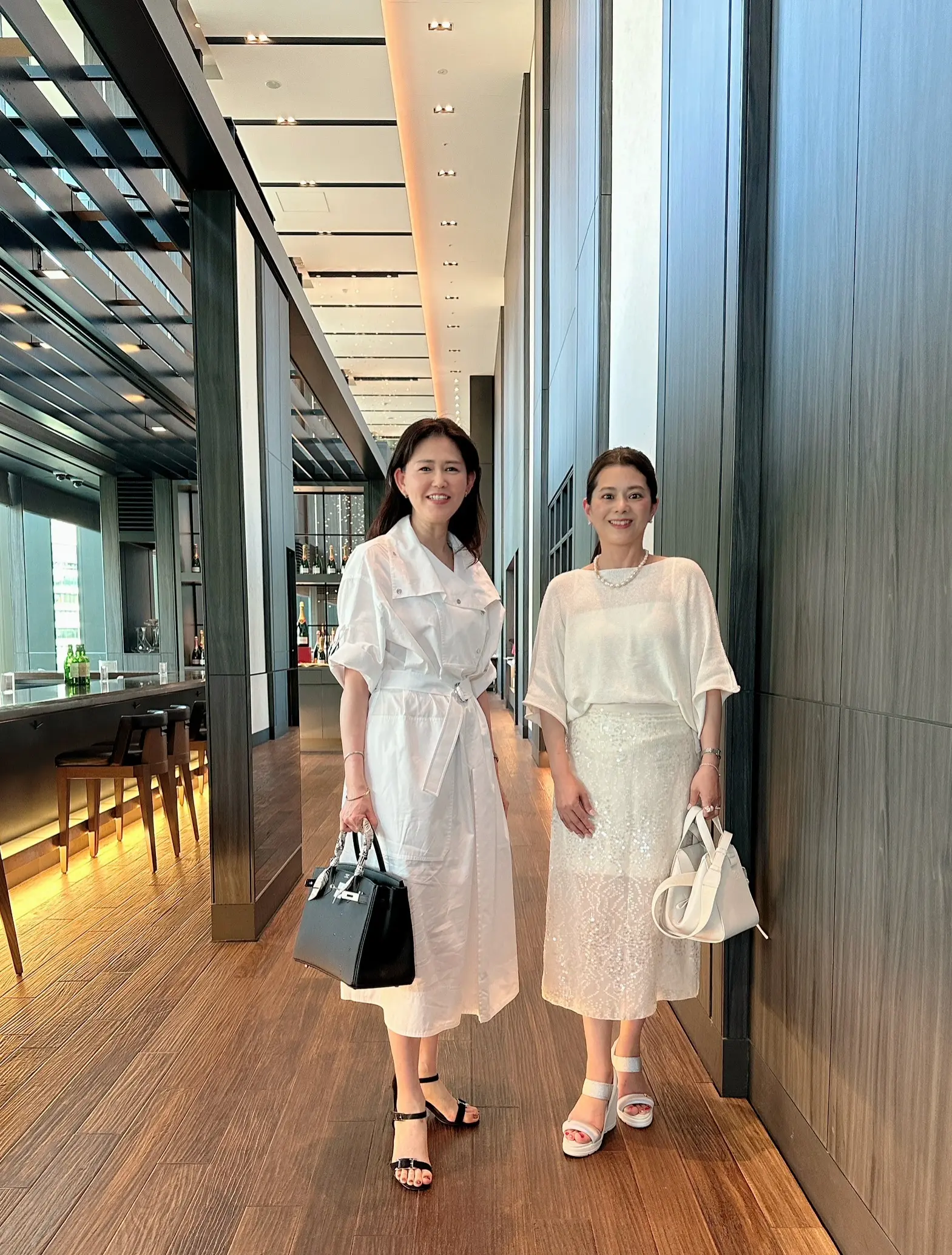 ホテルの廊下で並んで立つ2人の女性。どちらも白を基調とした上品な夏コーデ。
