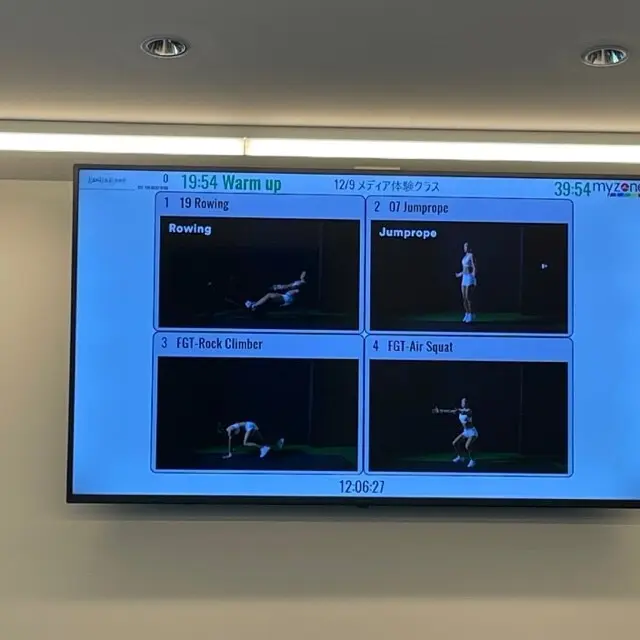 人気トレーナー・AYAさんのジムでのトレーニング中。正面スクリーンにそのトレーニングの動画が流されている