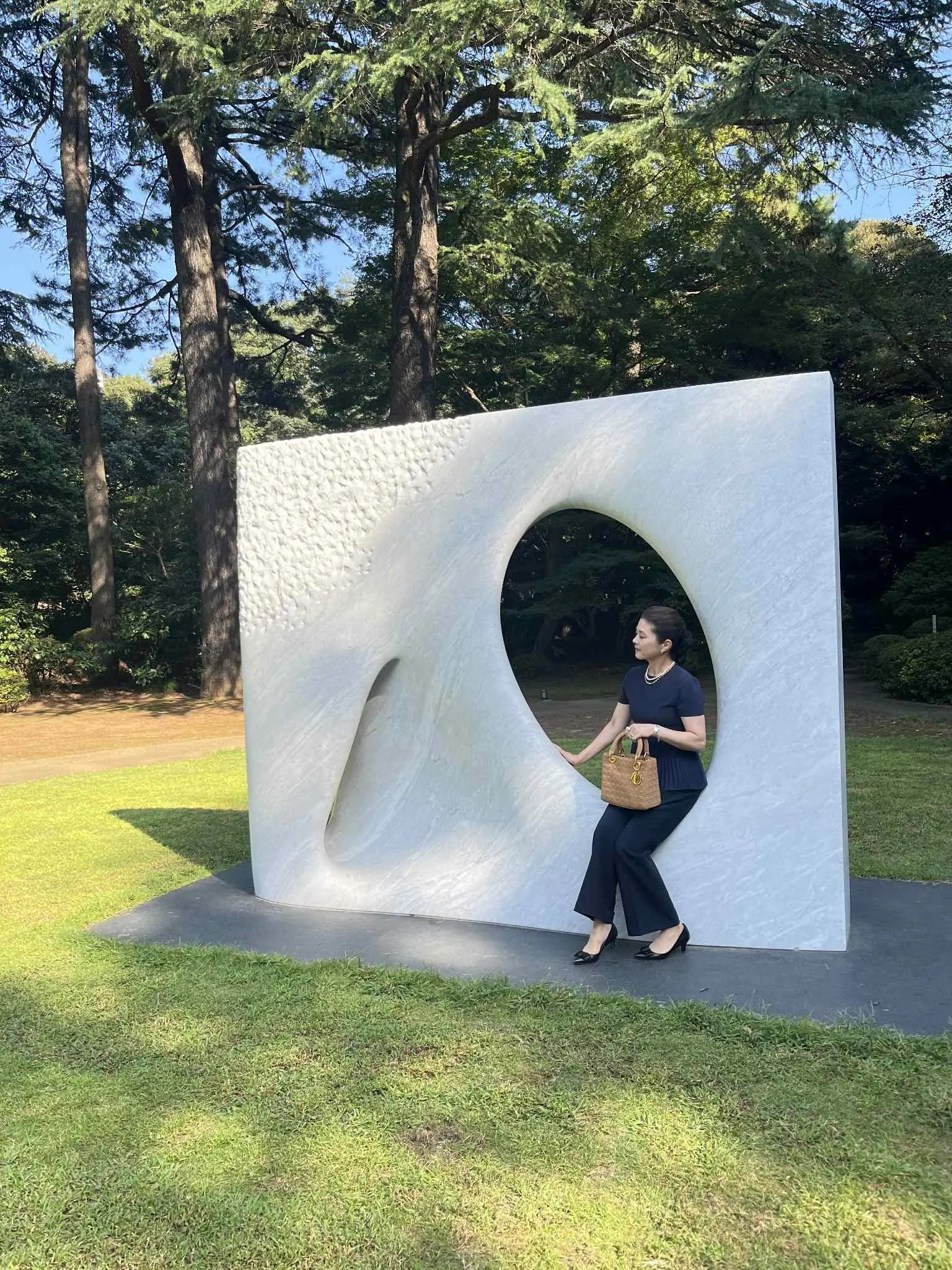 安田侃の彫刻《風》に腰掛け、柔らかな表情で遠くを見る女性。自然とアートが溶け合う空間。