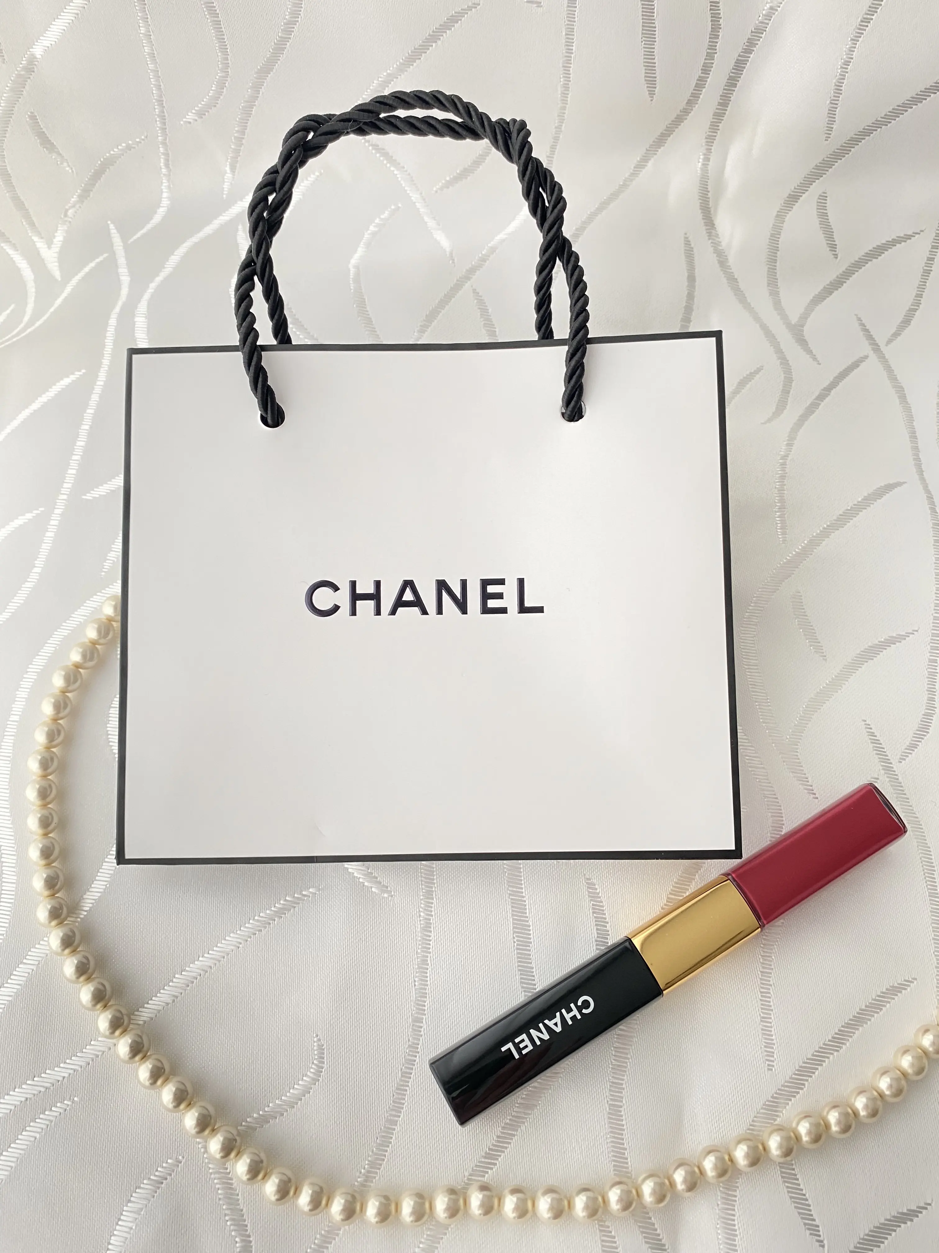 シャネルのショッパーと赤リップ、パールネックレスを組み合わせた上品なフラットレイ写真