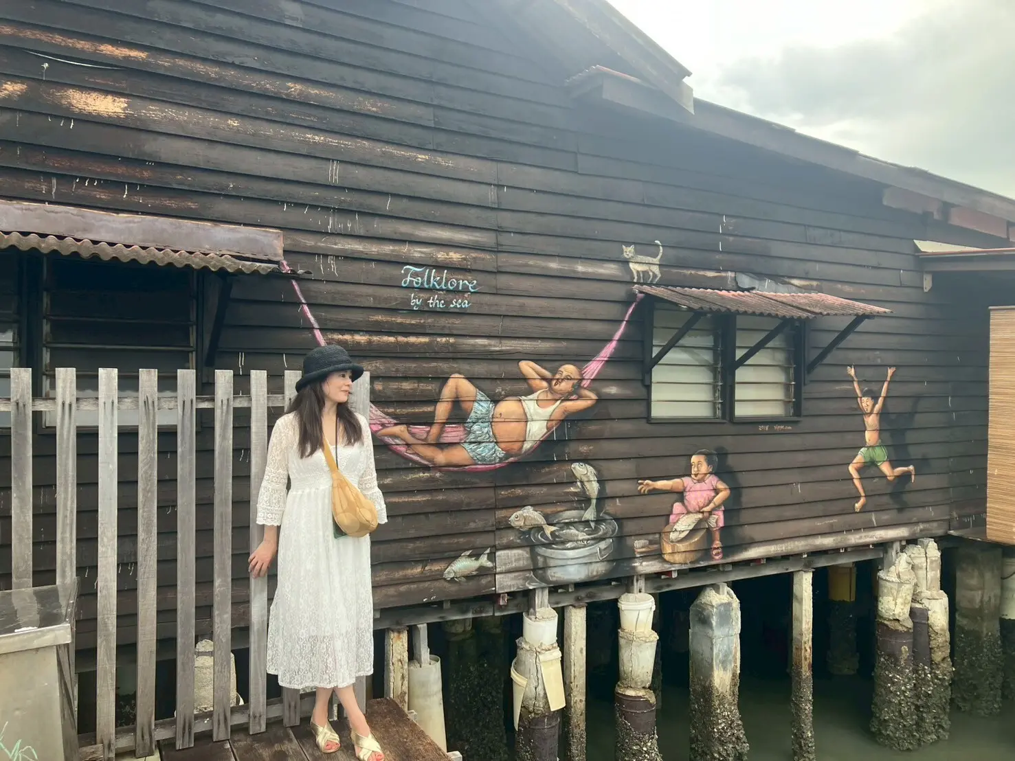 マレーシアペナン島Chew Jettyのウォールアート前で白いワンピース、ユニクロのバッグを持ちポーズを撮る女性