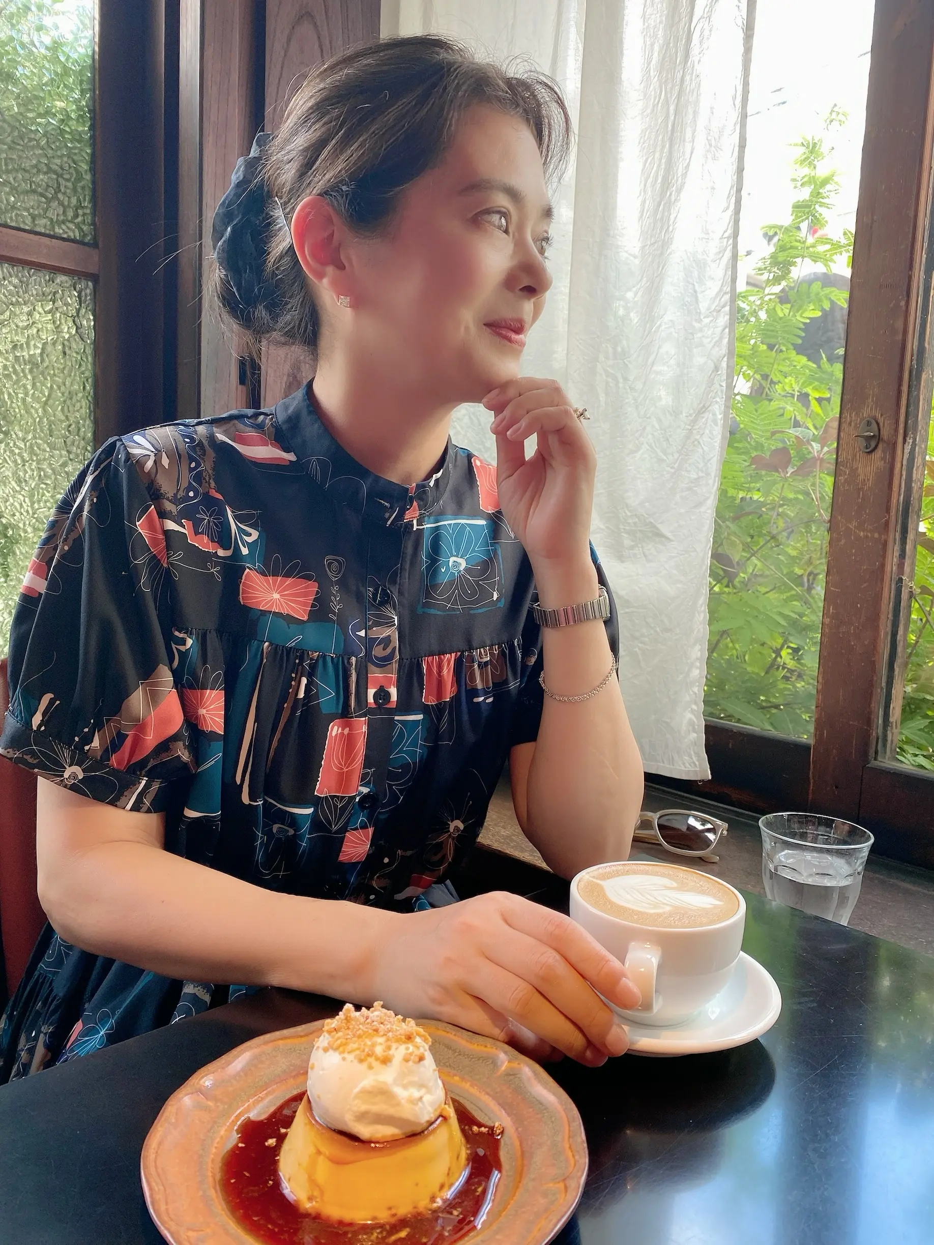 窓辺でカフェラテとプリンを楽しむ女性の横顔