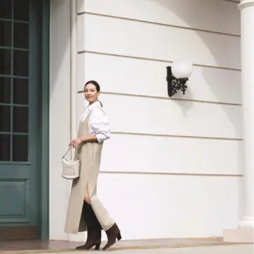スリットからロングブーツをのぞかせる旬なバランスで白×ベージュの上品配色をモードに仕上げる。気温19℃｜11/3(月)【50代の毎日コーデ】