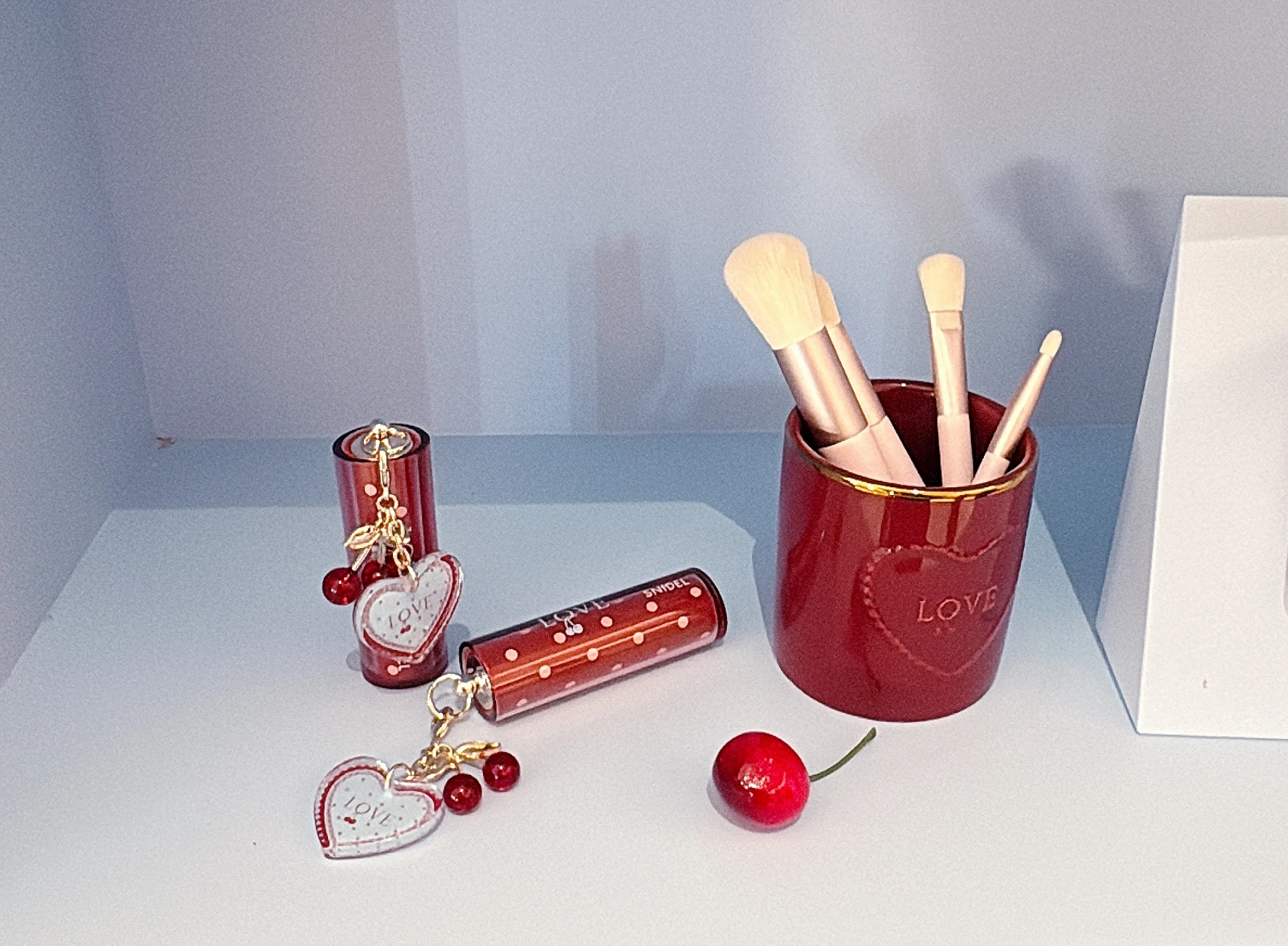 2026　新作コスメ　SNIDEL　左のルージュ クチュール（限定２種 各￥3520）も、じゃらっと可愛いチャームつき   なかでも手に入れたい！と思ったのは、チークブラシ、ハイライトブラシ、２本のアイシャドウブラシがセットになった、陶器スタンドつきのミニブラシセット。  天然毛のような柔らかさと絶妙なコシを両立した人工毛は、１本１本ウェーブ加工されているというこだわりっぷり。粉含みのよさも申し分なしだし、何よりダークチェリー×ホワイトのコントラストがこの上なくキュート。￥6600というプライスも魅力です。   こちらのバレンタインコレクションは、2026年1月7日(水)から予約スタート（オフィシャルオンラインストアでの予約・発売は午前10時より開始）。全国発売は2026年1月21日(水)ですのでお見逃しなく。