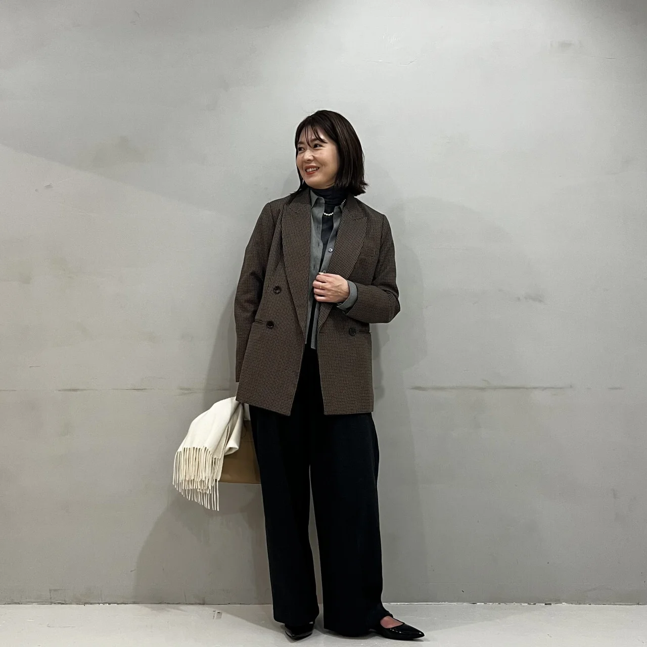 グレーのツイード風シャツ、ブラウンジャケット、黒パンツのコーデ