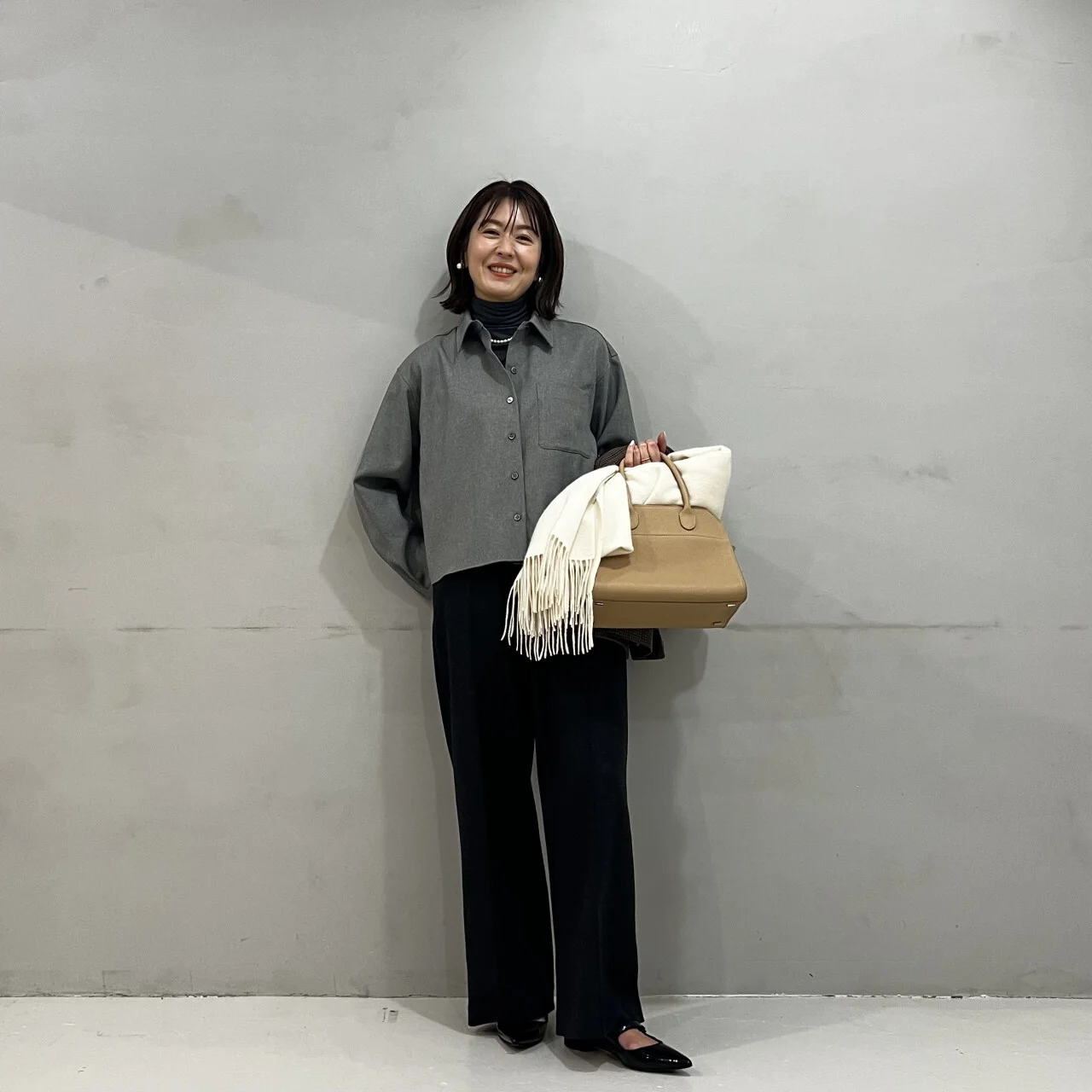 グレーのタートルと黒パンツのコーデにツイード風シャツを羽織っている