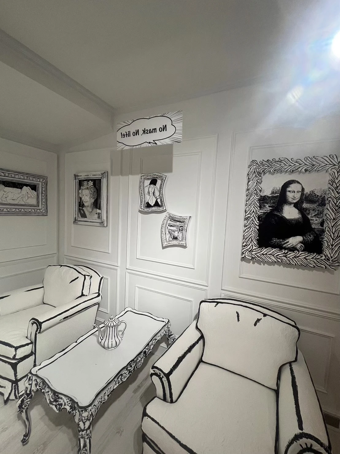 白黒の部屋の写真。ソファーや机があり、壁には絵が飾られている。