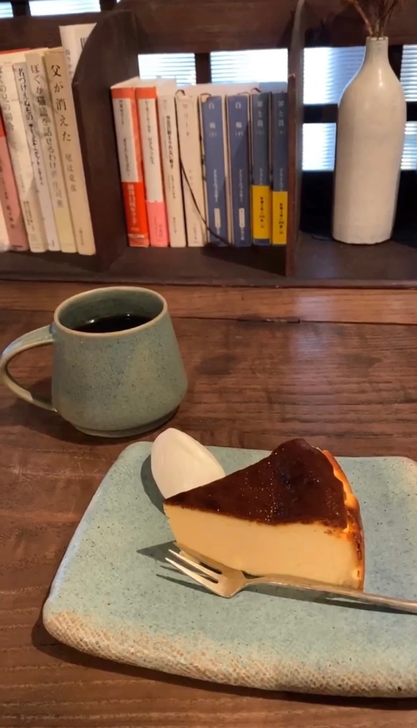 チーズケーキと珈琲。きの机の上には、木で作られた本棚と花瓶が置かれています。