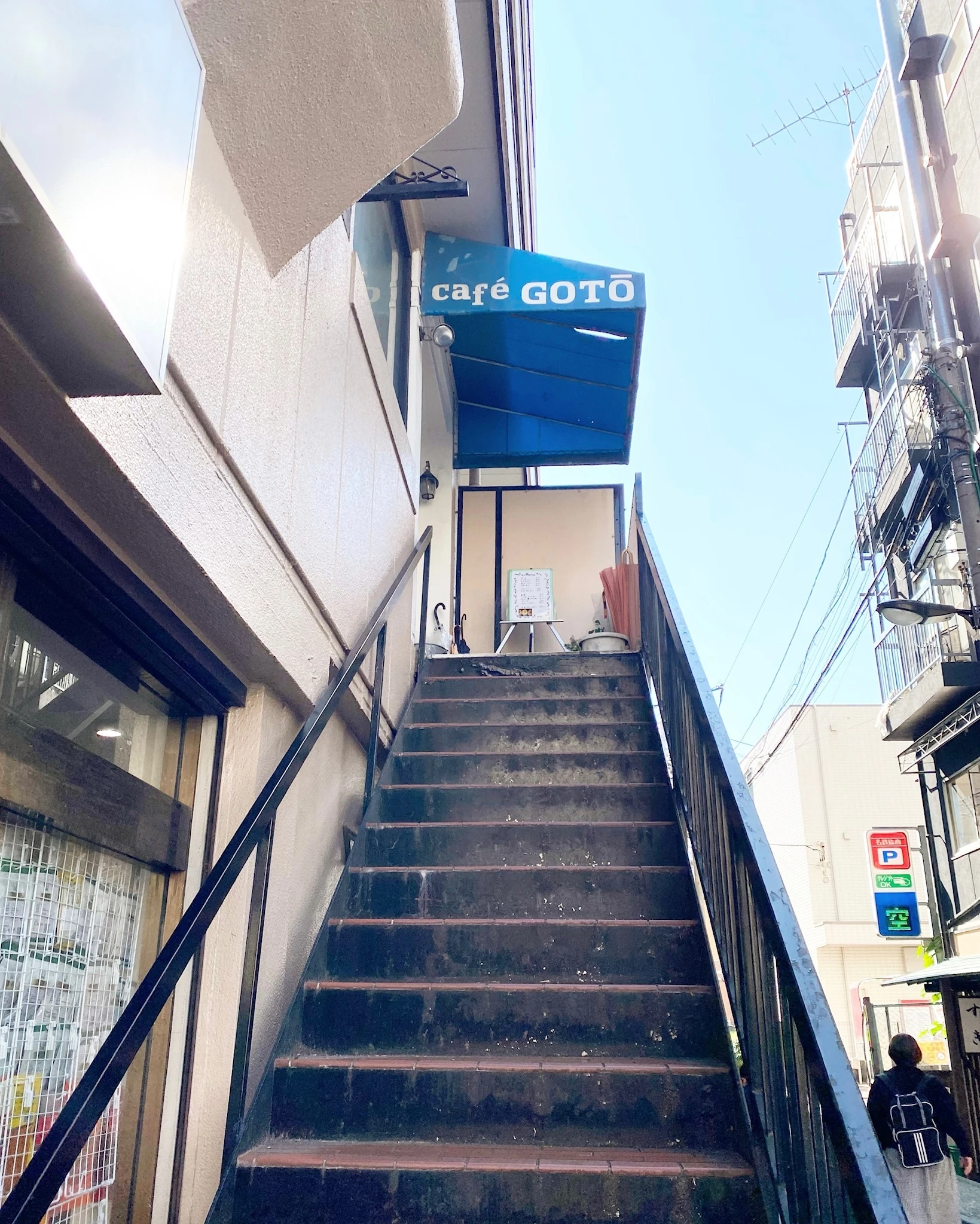 早稲田駅から徒歩2分のところにある喫茶店「cafe GOTO」の外観。
店舗のある二階へ伸びる階段がある。店の入り口部分には、青い屋根がついており、「cafe GOTO」という白い文字が入っている。