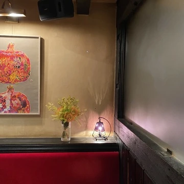 神保町にある喫茶店「トロワバグ」の店内。赤い絨毯のような生地のソファと、大きな絵、花瓶に生けられたオレンジや白、黄緑を基調としたお花、紫色のガラスが使われたライトが置かれています。